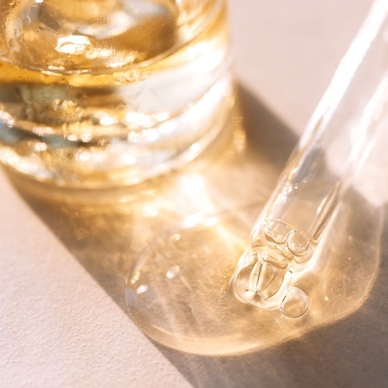 Detail skleněné pipety s kapkou pleťového séra s obsahující aktivní látky jako kyselina hyaluronová a retinol, vitamin C, bakuchiol..