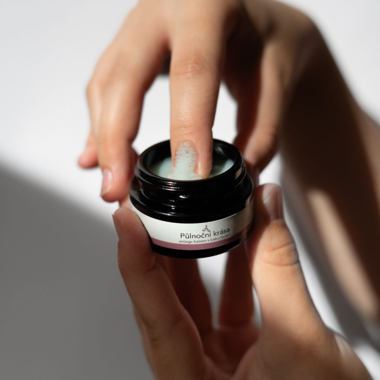 žena sahající do dózičky, nabírající půlnoční krásu nehtem