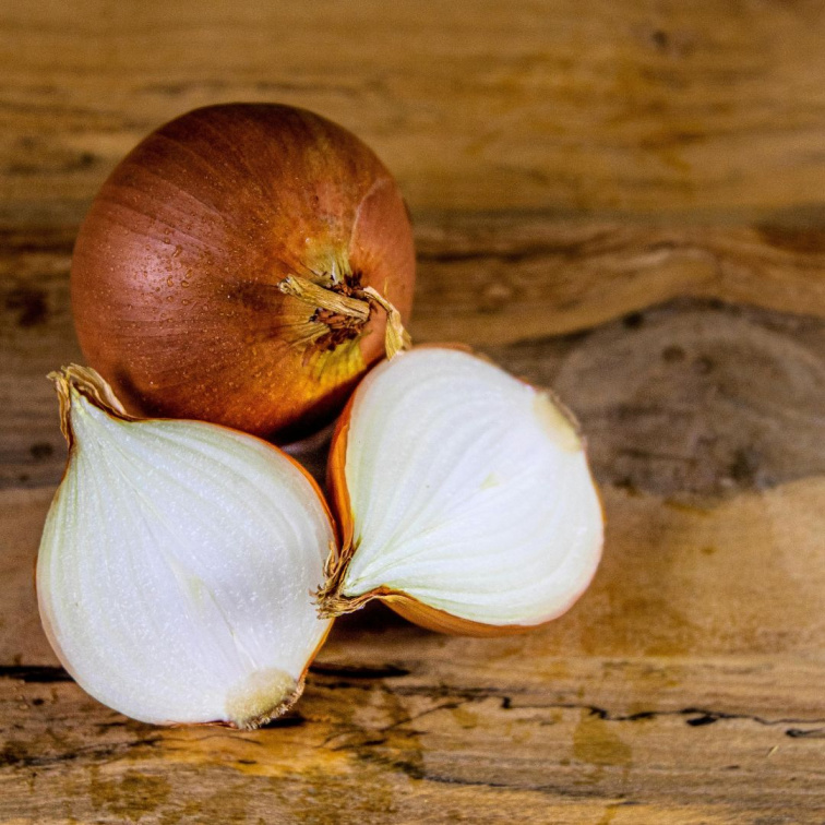 Rozkrojená cibule na dřevěném prkénku jako tradiční domácí první pomoc při bodnutí hmyzem.