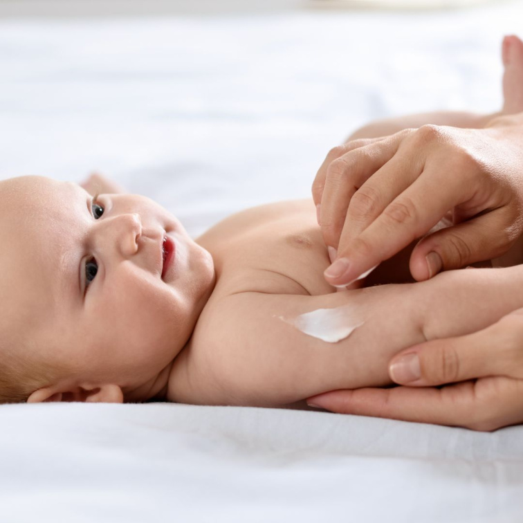 Nanášení ochranného opalovacího krému s vysokým SPF 50+ na ručičku ležícího miminka.