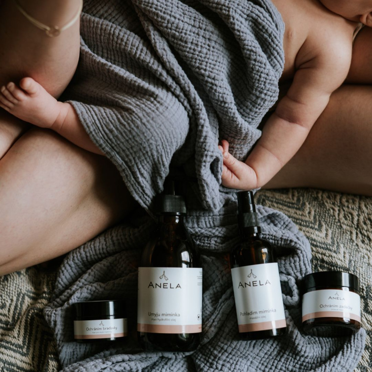 miminko ležící v matčině klíně, v popředí kosmetické dětské produkty