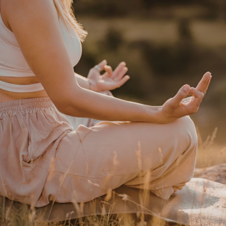 Žena sedící v meditační pozici lotosového květu v přírodě během západu slunce pro snížení stresu a zklidnění atopické kůže.