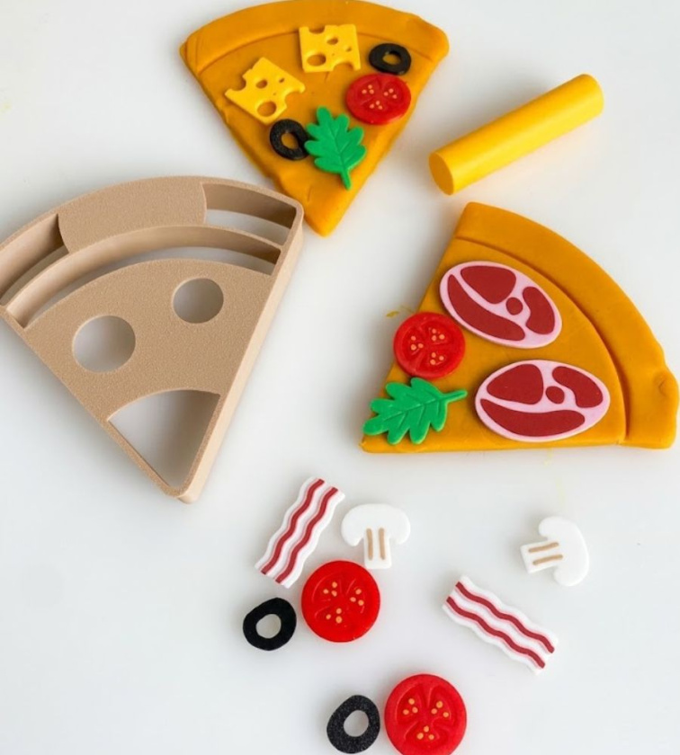 Vykrajovátka na modelínu pizza. Vykrojený kousek modelíny Mámy v rejži a na něm drobnosti pro dotvoření z kreativní modelínové sady Pizza.