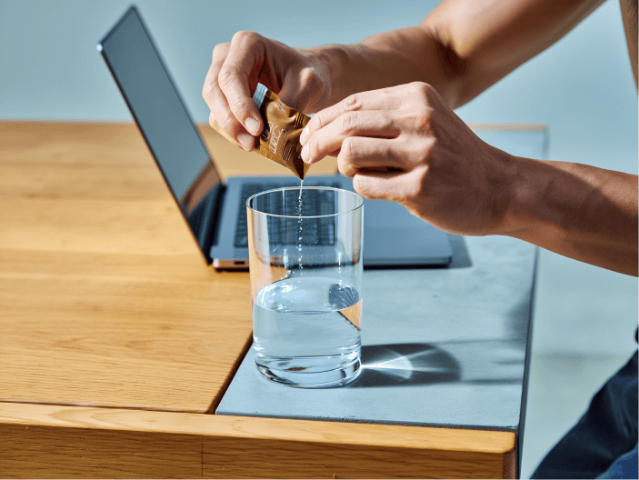 Muž sype kolagen ZAYRAĒ MAN do pohára s vodou