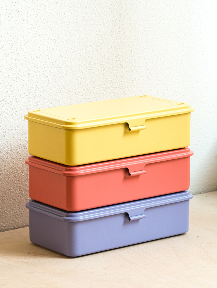 Kovové úložné boxy Toyo Steel T190 ve žluté, korálové a světle fialové barvě, naskládané na sobě u světlé zdi
