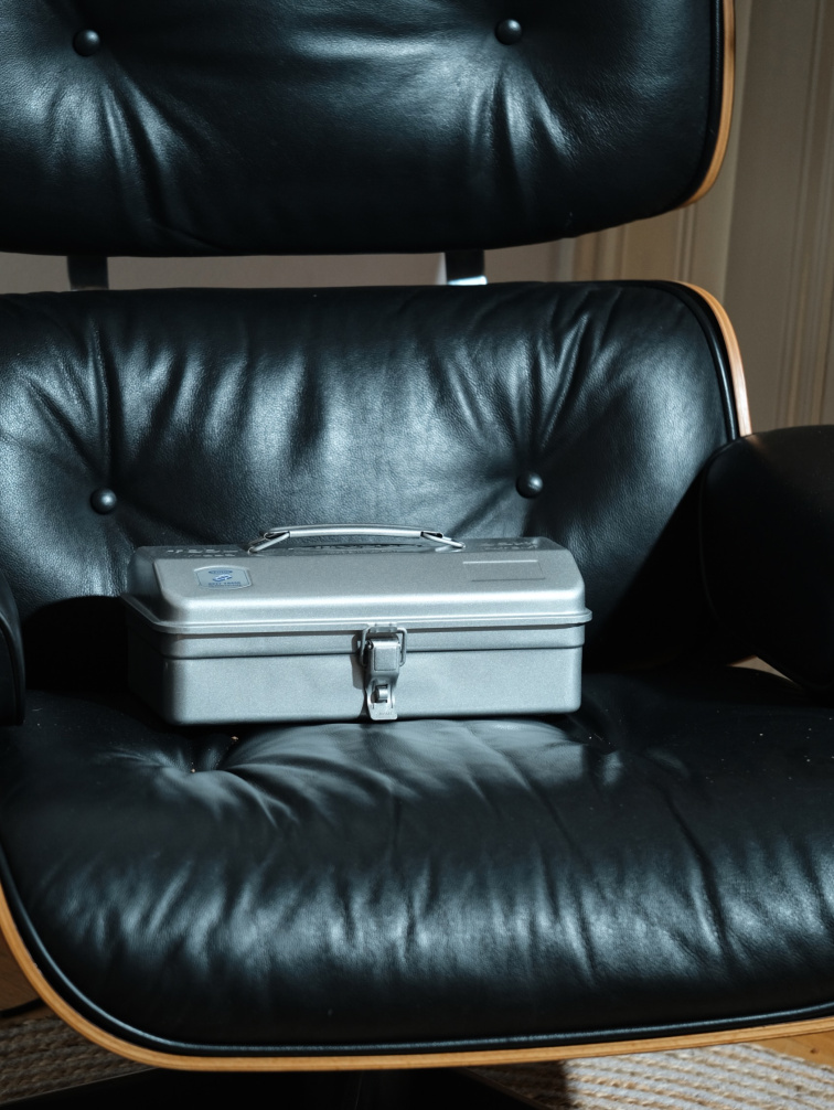 Kovový box Toyo Steel Y280 stříbrný položený na kožené židli Eames